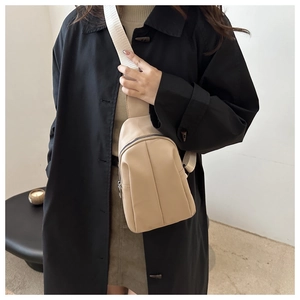 Close-up of minimalist beige PU leather chest bag with a wide white fabric shoulder strap