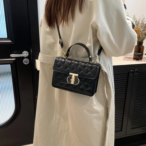 Minimalist black quilted crossbody bag with gold T-clasp hardware and leather handle