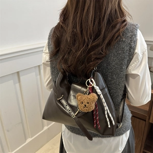 Sac bandoulière en cuir marron foncé avec pendentif ours, porté par un mannequin en intérieur