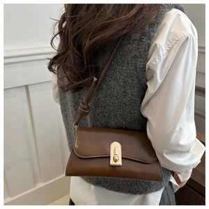 Detail of dark brown polished leather shoulder bag featuring a gold twist-lock closure