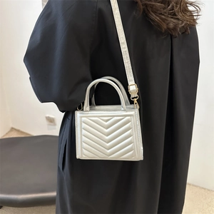 Silver V-quilted small crossbody bag with top handle shown on model in black coat