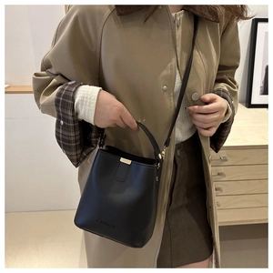 Detail of a black leather bucket bag with gold hardware worn with a beige trench coat