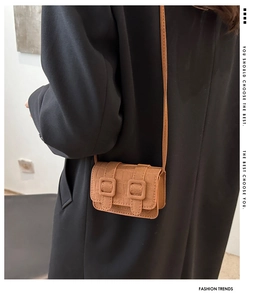 Detail of brown faux leather crossbody bag with square embossed pattern and decorative buckles