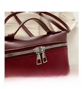 Detail of burgundy dual-zipper closure and suede stitching on minimalist bucket bag