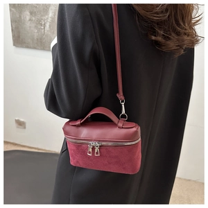 Close-up of a burgundy leather bucket bag with suede patchwork and silver zippers