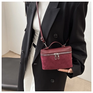Detail of burgundy leather mini bucket bag featuring dual silver zippers and mixed textures