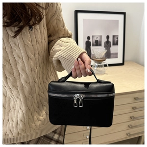 Detail of minimalist black leather bucket bag with silver zippers held by a model