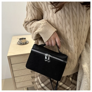 Close-up of a black bucket bag featuring textured patchwork and silver double zippers