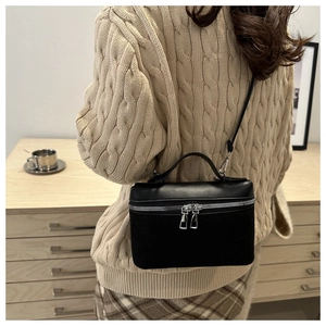 Close-up of a black matte leather box crossbody bag worn over a beige sweater