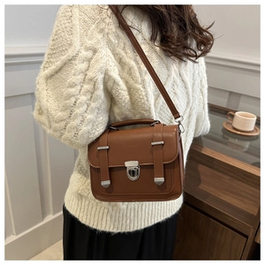 Brown retro leather crossbody bag with silver lock worn by a model in a cozy room