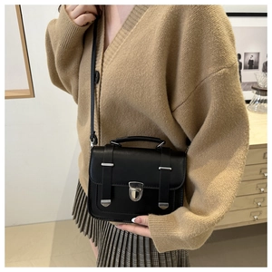 Close-up of black retro handbag with silver buckle and crossbody strap on a model