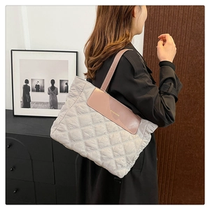 Detail view of quilted tote bag with pink-brown leather handles and FASHION logo text