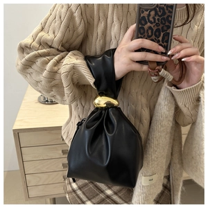 Close-up of black pleated bucket bag featuring an artistic gold pebble-shaped buckle detail