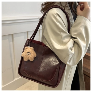 Détail d'un cabas vintage bordeaux en cuir brillant avec un petit charme d'ours en peluche
