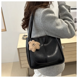 Détail d'un grand sac cabas noir avec pendentif ours, porté sur un blazer en laine gris