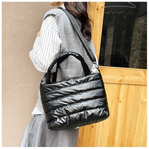 Close-up of black quilted puffer tote bag with glossy nylon texture and wide crossbody strap