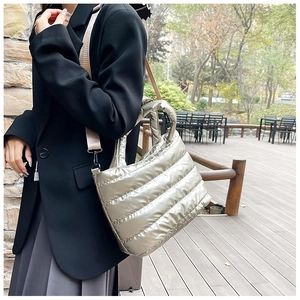 Metallic quilted crossbody bag with wide shoulder strap shown in a lifestyle park setting