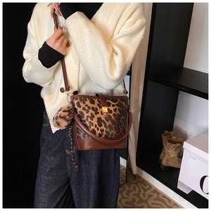 Detail shot of leopard print bucket bag with brown leather trim and plush charm on model