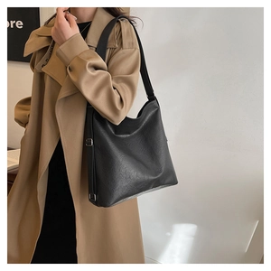 Detail of a large black tote bag with textured leather and silver buckle on a trench coat