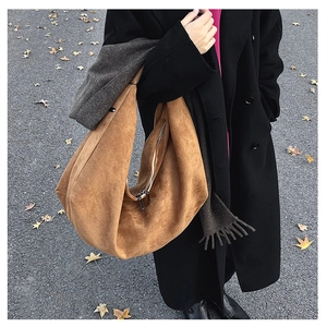 Close-up of caramel suede hobo tote bag with a metallic zipper on autumn street