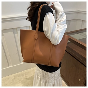 Side view of a large brown faux leather tote bag worn by a model for a stylish look