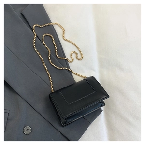 Detail of minimalist black square bag with gold chain strap on a grey suit jacket
