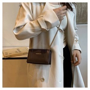 Detail of dark brown square bag with gold chain strap on a white coat model