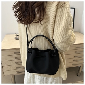 Detail einer schwarzen Beuteltasche mit Ringgriff, getragen von einem Model im Innenraum