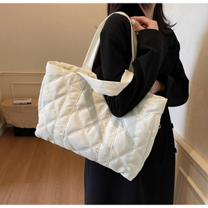 Dettaglio della borsa tote trapuntata bianca con motivo a rombi su cappotto nero