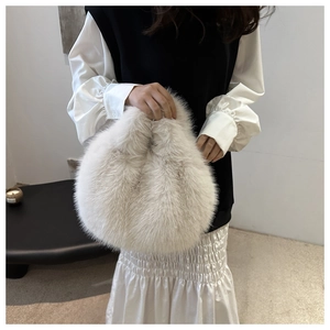 Detailed view of a soft cream faux fur round handbag held by a model for winter fashion