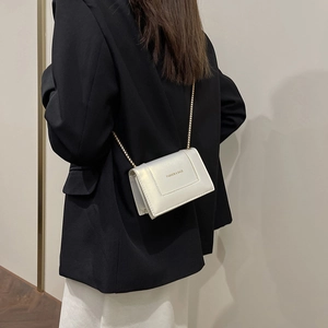 Elegant ivory white crossbody chain bag with gold lettering shown on a female model