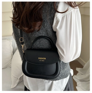 Detail of black leather saddle bag featuring a gold fashion logo and crossbody strap