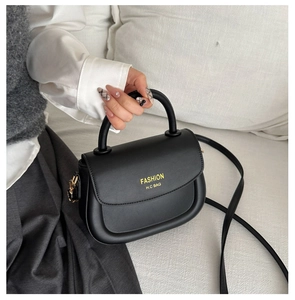 Close-up of black leather saddle bag featuring gold fashion lettering and top handle