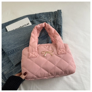 Detail of pink quilted shoulder bag with golden bow hardware on soft puffer material