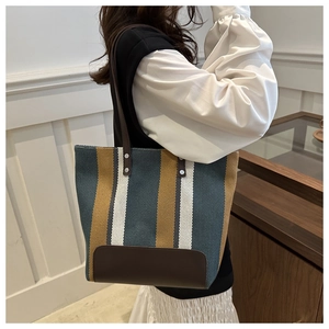 Detailed side view of large striped canvas tote bag with brown leather handles on model