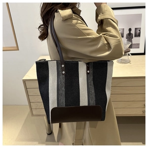 Vertical striped fabric tote bag with brown leather handles worn over the shoulder