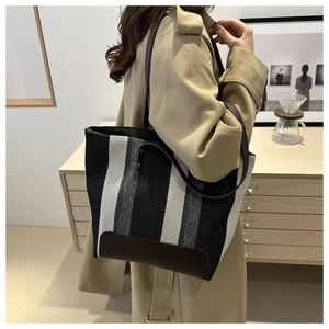 Detail of a striped canvas tote bag featuring premium brown leather trim and handles