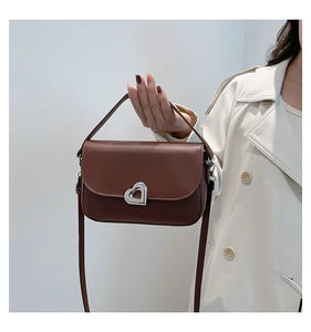 Detailed view of brown leather saddle bag with silver heart lock and crossbody strap