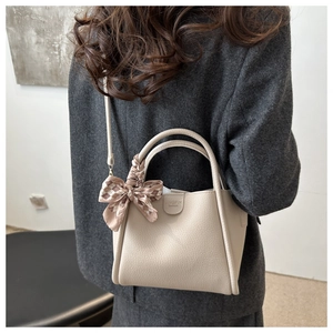 Detail of beige lychee leather bucket bag featuring a plaid bow and crossbody strap