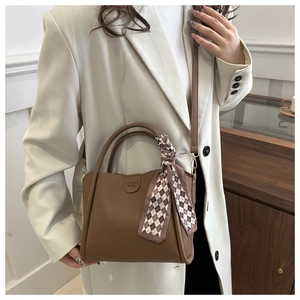 Détail du sac à main marron en cuir grainé avec foulard à carreaux chic sur la poignée