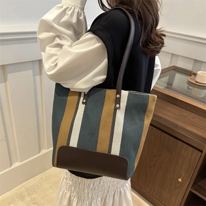 Vertical striped tote bag in woven canvas with brown leather straps worn by a female model