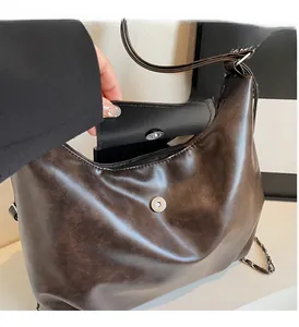 Detail of dark brown glossy hobo bag with silver magnetic flap and leather-interwoven chain
