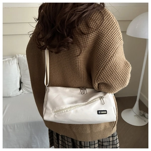 Détail d'un sac bandoulière crème en cuir avec fermeture éclair et étiquette mode