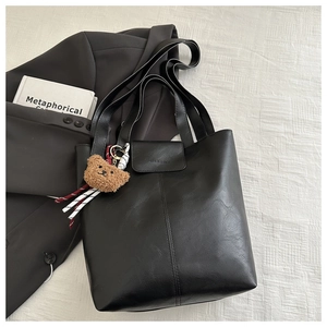 Detail of black faux leather tote bag with embossed fashion text and brown bear charm