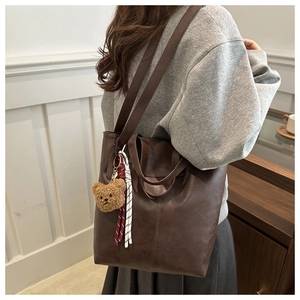 Detail of dark brown matte leather tote bag featuring fashion embossing and bear charm