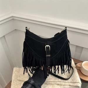 Retro black suede crossbody bag with long fringes and golden buckle in a cozy setting