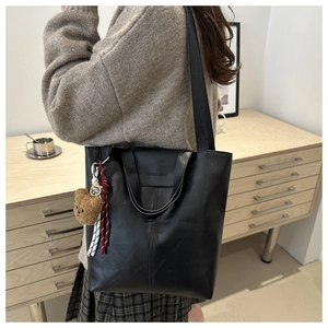Detail of black tote bag with long straps, logo print and brown plush bear charm