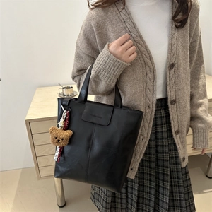 Fashionable black faux leather tote bag with bear charm and top handle strap