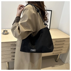 Detail of black suede hobo bag featuring knotted shoulder strap and leather logo patch
