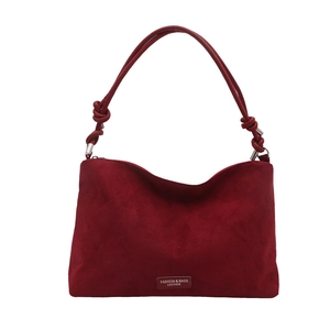 Deep red suede tote bag with knotted strap and metal logo plate on a white background